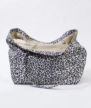 A soft fabric tote bag with a navy blue leopard print pattern on a cream background, featuring a beige interior lining and a matching shoulder strap, set against a plain white studio background.