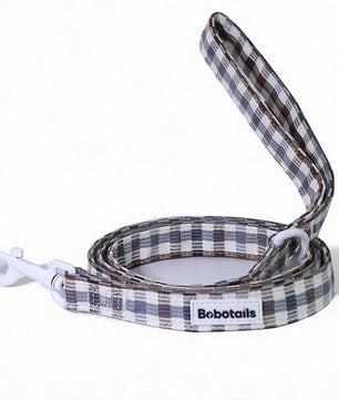 A plaid dog leash with a white clip and white D-rings, featuring a white label with the brand name 'Bobotails'. The leash has a  pattern of brown, gray, and white plaid, shown on a clean white background.