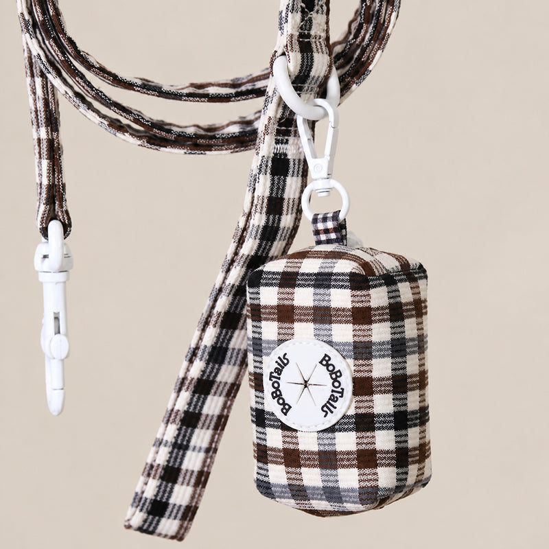 A brown, black, and beige plaid dog leash and matching bag set with white hardware, featuring a circular 'Bobotails logo patch on the bag, set against a solid beige background.