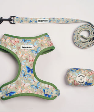 A pet leash set with a matching harness, leash, and zippered pouch on a light gray background. The set features a pastel butterfly and floral pattern on a sage green base, with sage green trim.