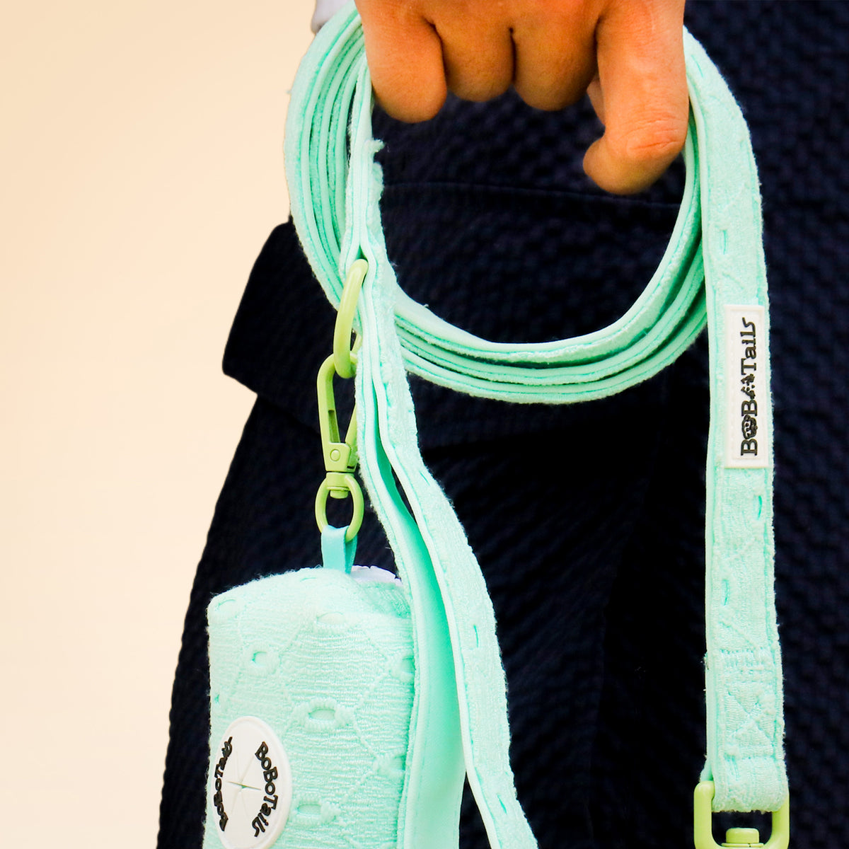 Mint green dog leash with a holder, held by a person against a beige background.