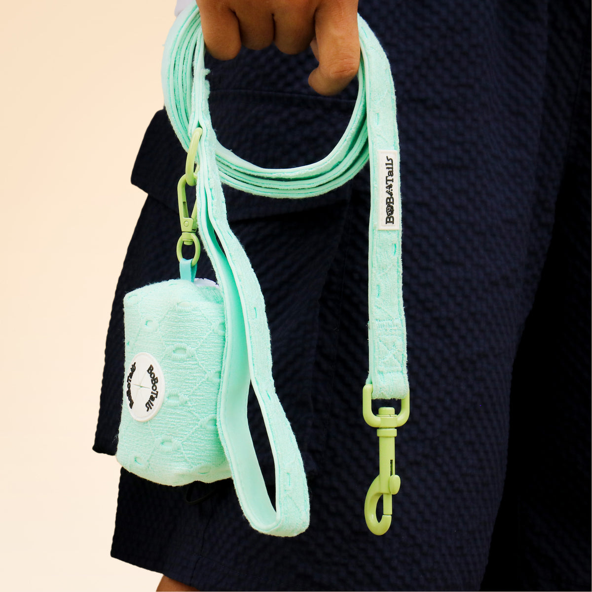 Mint green dog leash and pouch held by a person wearing a textured navy sweater.
