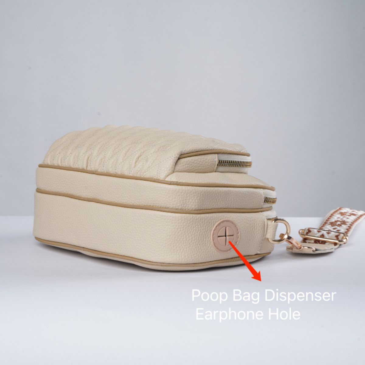Beige handbag with a poop bag dispenser and earphone hole on a light gray background