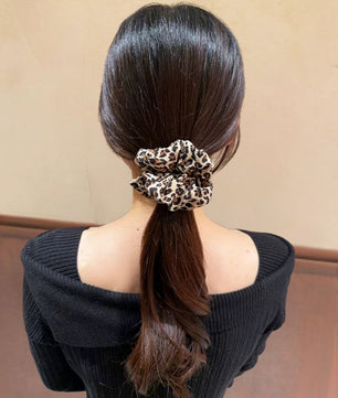 Person with a ponytail wearing a leopard print scrunchie against a beige background