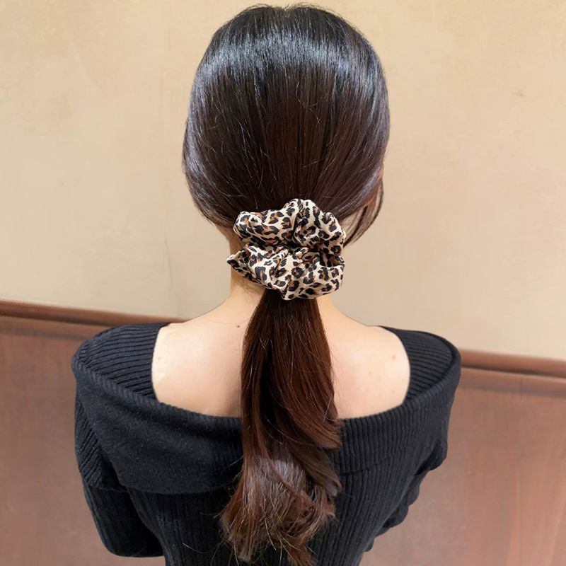 Person with a ponytail wearing a leopard print scrunchie against a beige background