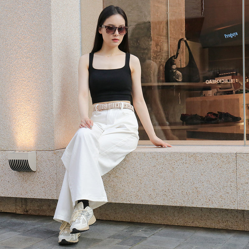 Woman in black top and white pants sitting on a ledge with a store window in the background